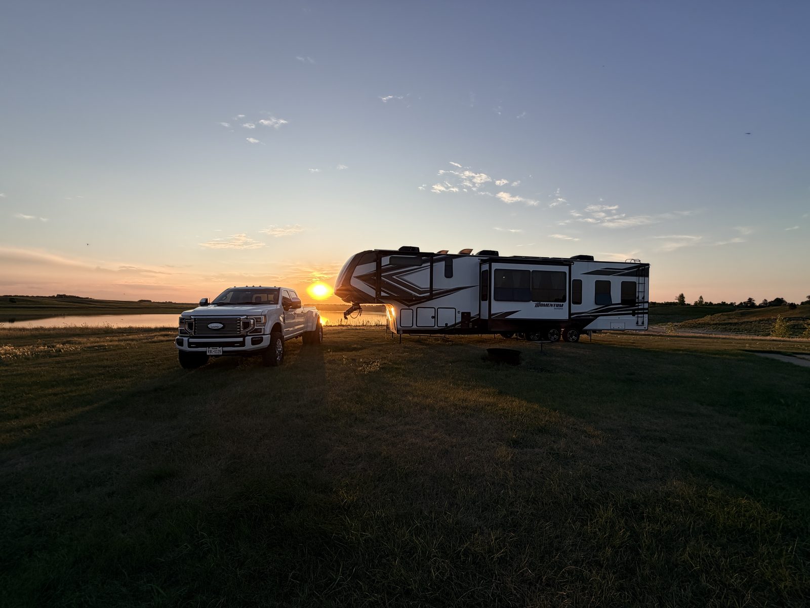 A white truck and fifth wheel parked by a lake at sunset